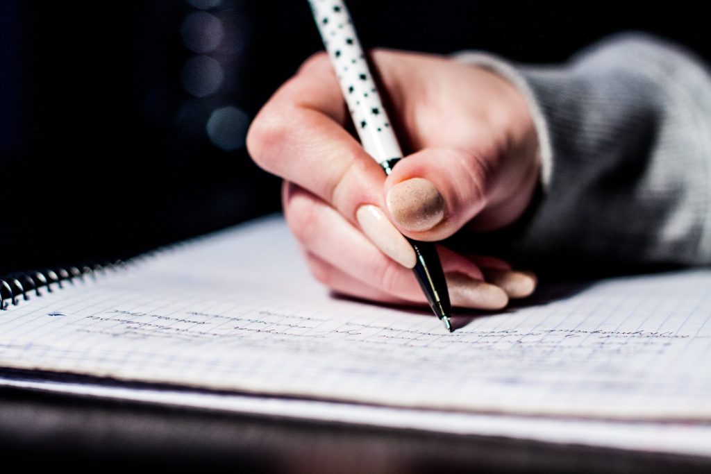 rechte Hand mit schwarz-weiÃŸen Sternchenkugelschreiber, die auf einem karierten Block schreibt.