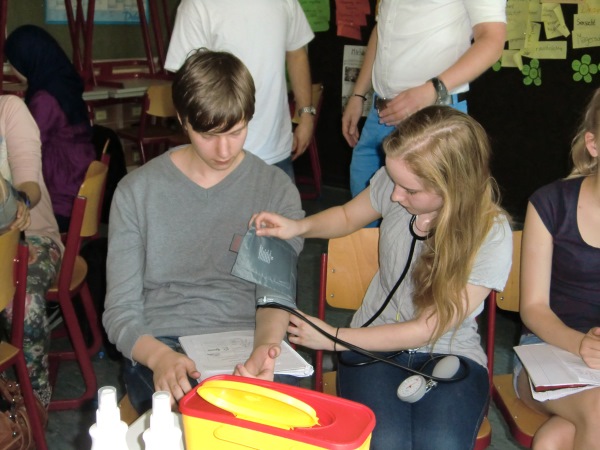 SchÃ¼ler beim Berufsinformationstag. Eine SchÃ¼lerin mit einem Stethoskop legt einem SchÃ¼ler eine Blutdruckmanschette an.