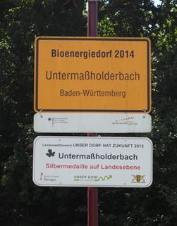 gelbes Ortsschild des Bioenergiedorfs UntermaÃŸholderbach Baden - WÃ¼rttemberg darunter ein weiteres weiÃŸes Schild mit der Aufschrift "Landeswettbewerb UNSER DORF HAT ZUKUNFT 2015" UntermaÃŸholderbach Silbermedaille auf Landesebene