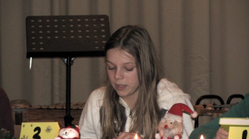 Eine Schülerin liest beim Vorlesewettbewerb vor. Vor ihr steht ein gelbes Schild mit der Zahl drei und ein Nikolaus. Im Hintergrund steht ein schwarzer Notenständer