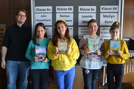 Die am Vorlesewettbewerb teilnehmenden Schülerinnen stehen vor einer Stellwand mit ihren Namen, in ihren Händen halten sie die von ihnen gelesenen Bücher, neben ihnen steht ein Lehrer.