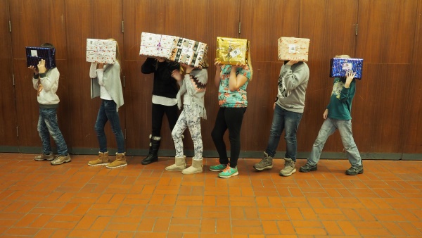 sechs SchÃ¼lerinnen und SchÃ¼ler halten weihnachtlich verpackte Schuhkartons vor ihrem Kopf.