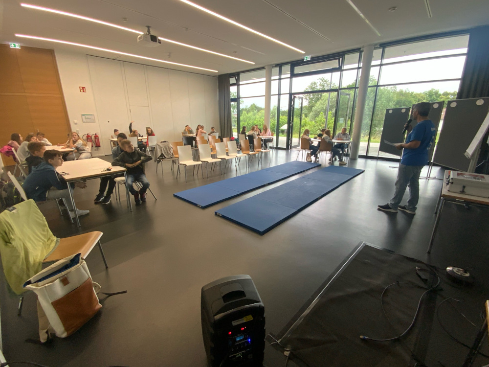 Es wird gezeigt, wie der Schulsozialarbeiter Herr Böhm im Jugendpavillon mit einer Klasse ein Sozialtraining durchführt.