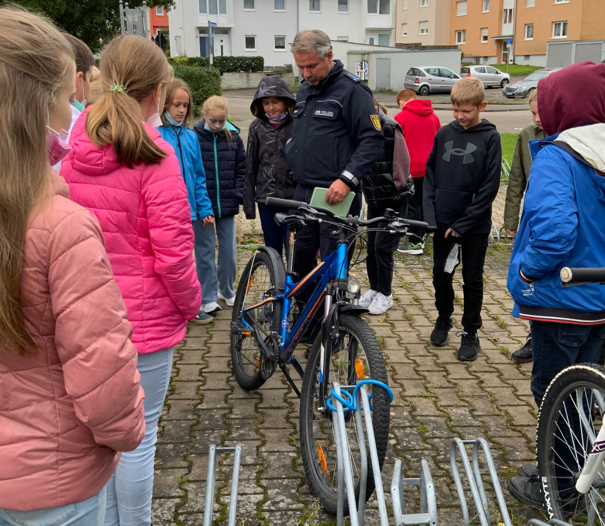Ein Polizist erklÃ¤rt auf dem Parkplatz SchÃ¼lerinnen und SchÃ¼lern die Bestandteile eines verkehrssicheren Fahrrads