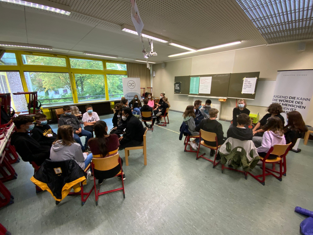 SchÃ¼lerinnen und SchÃ¼ler sitzen jeweils in Kleingruppen im Stuhlkreis und arbeiten mit den Workshop-Leitern