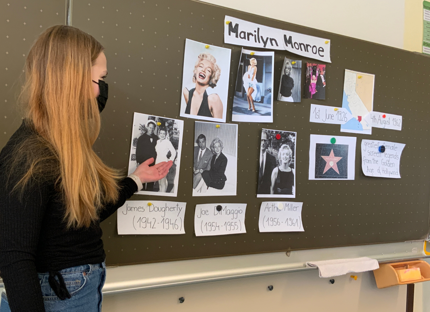 SchÃ¼lerin steht vor der Tafel an der sich Materialien zu ihrer PrÃ¤sentation Ã¼ber Marilyn Monroe befinden